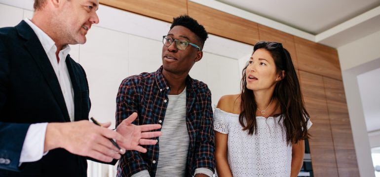 Interracial couple having consultation with a real estate agent inside a home for sale. Concept of working with a real estate agent rather than listing "For Sale By Owner."