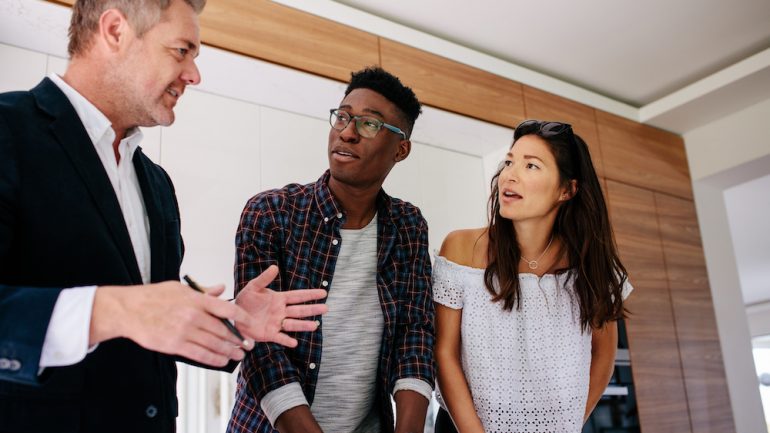 Interracial couple having consultation with a real estate agent inside a home for sale. Concept of working with a real estate agent rather than listing "For Sale By Owner."