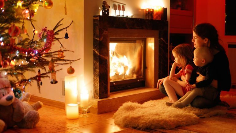 Mother and children in front of warm and cozy fireplace during Holiday season.