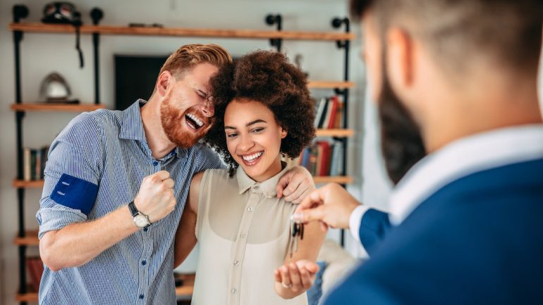 Real estate agent giving house keys to couple in their new home.