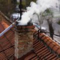A red tile roof top with a chimney blowing white smoke.