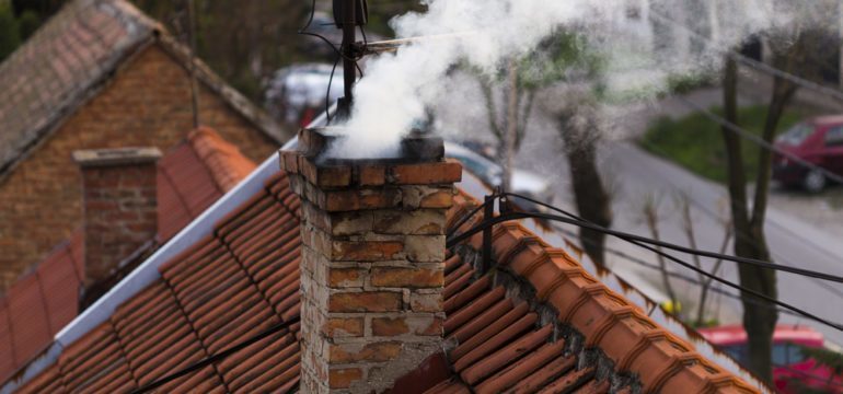 A red tile roof top with a chimney blowing white smoke.