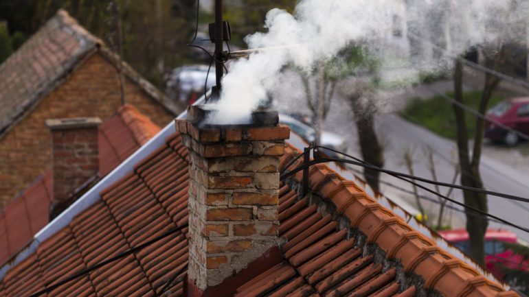 A red tile roof top with a chimney blowing white smoke.