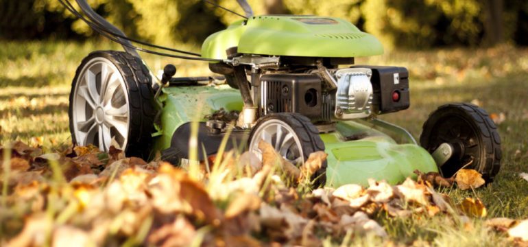 Green lawn mower in the garden at autumn sunset. Leaf removal and final mowing are on October home maintenance tasks.