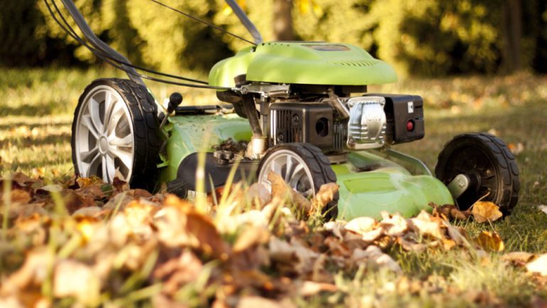 Green lawn mower in the garden at autumn sunset. Leaf removal and final mowing are on October home maintenance tasks.
