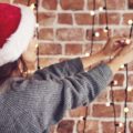 Woman with Santa hat stringing Christmas lights as part of her December To-Do list.