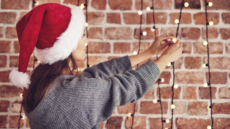 Woman with Santa hat stringing Christmas lights as part of her December To-Do list.