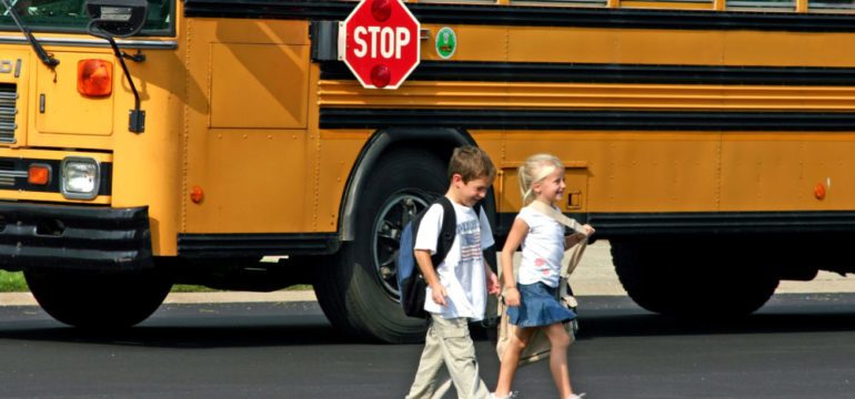 Kids crossing the street in front of school bus to show the difference between public and private streets.