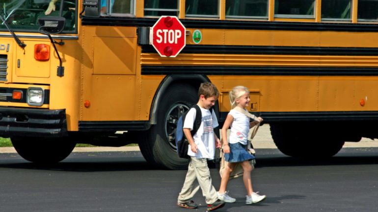 Kids crossing the street in front of school bus to show the difference between public and private streets.