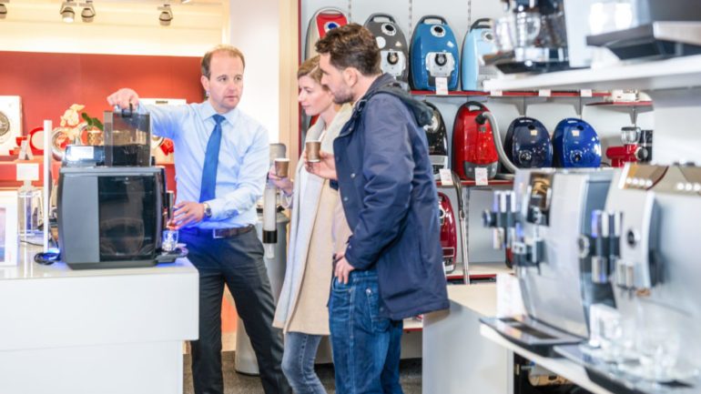 Salesman showing coffee maker to young couple in electronics store for June specials.