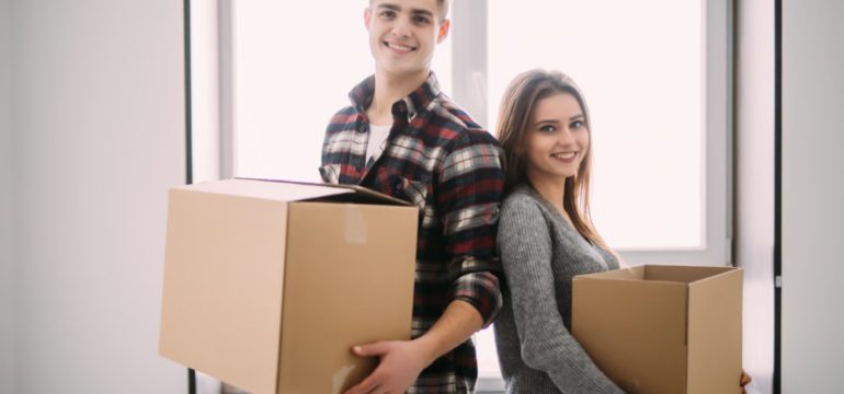 New home buyer couple holding boxes moving into their first home.