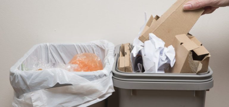 Hand puts cardboard into home trash bin