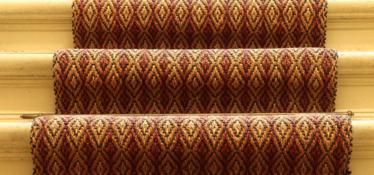 Textured carpet runners in red and gold pattern on light hardwood stairs.