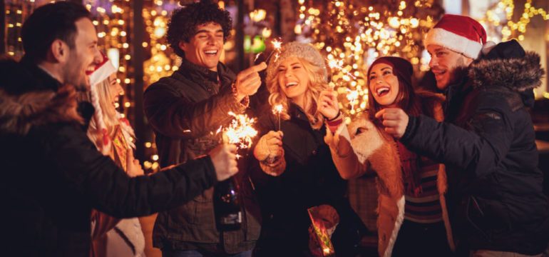 Three couple with sparklers enjoying Christmas block parties in the neighborhood street at night and with a lot of lights on background.