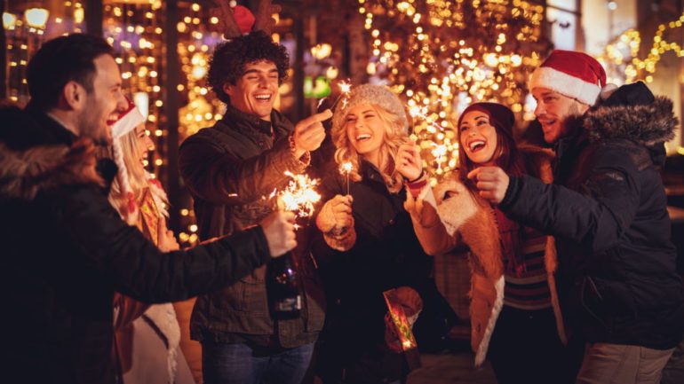 Three couple with sparklers enjoying Christmas block parties in the neighborhood street at night and with a lot of lights on background.