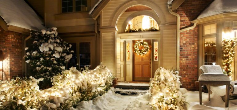 Outdoor Christmas decorations line path to a front door on a snowy evening.