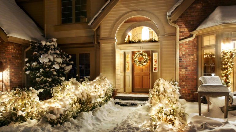 Outdoor Christmas decorations line path to a front door on a snowy evening.