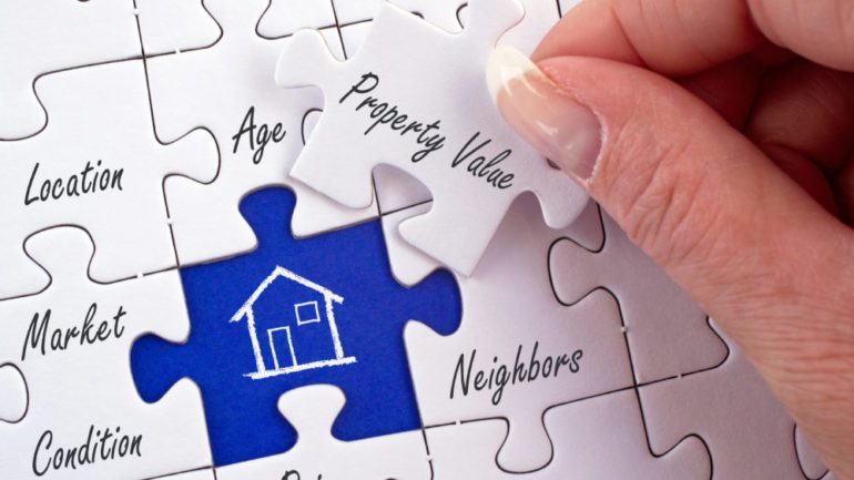 Property value and home equity puzzle with female hand placing piece in a real estate puzzle.