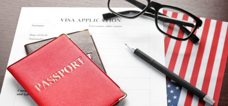 Passports, visa application form and American flag on table representing items needed when trailing spouses relocate.