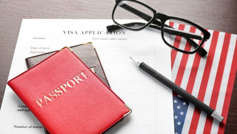Passports, visa application form and American flag on table representing items needed when trailing spouses relocate.
