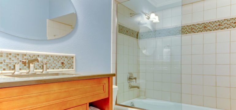 New bathroom with blue walls and white bathtub. Shows shower glass panel instead of shower curtain.