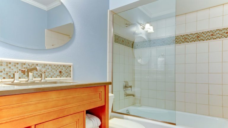 New bathroom with blue walls and white bathtub. Shows shower glass panel instead of shower curtain.