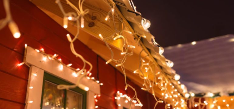 Outdoor Christmas lights around windows and roof lines of red house with white trim.