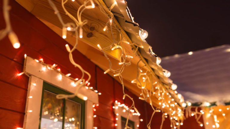 Outdoor Christmas lights around windows and roof lines of red house with white trim.