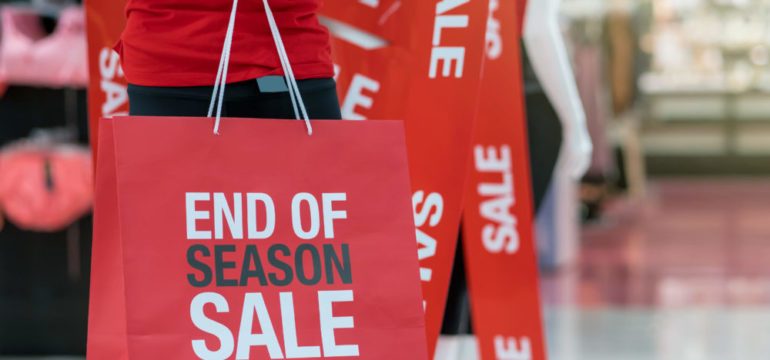 Part of male mannequin dressed in casual clothes holding the sales paper shopping bag to show best buys for December.