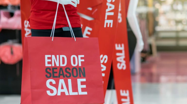 Part of male mannequin dressed in casual clothes holding the sales paper shopping bag to show best buys for December.