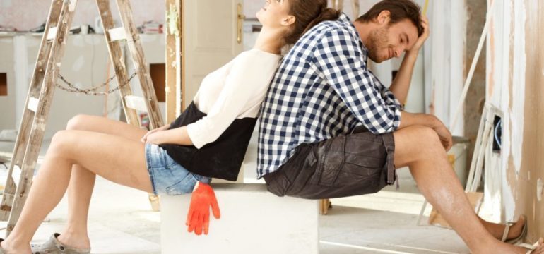 Exhausted DIY couple sitting in house under construction back to back.