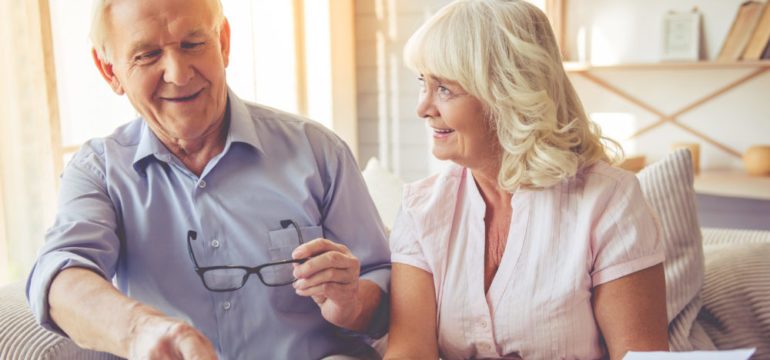 Handsome old man and beautiful woman are discussing home resizing project and smiling while sitting on couch.