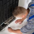 Young male repairman making repairs to home refrigeration appliance In kitchen.