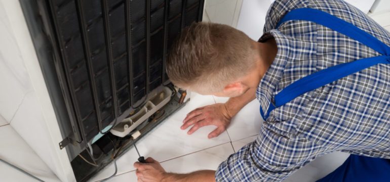 Young male repairman making repairs to home refrigeration appliance In kitchen.