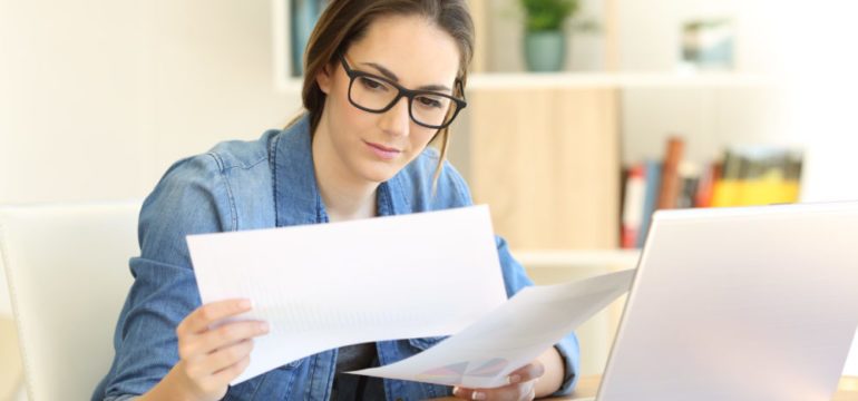 New homeowner comparing closing documents for storage on a table with her laptop open.