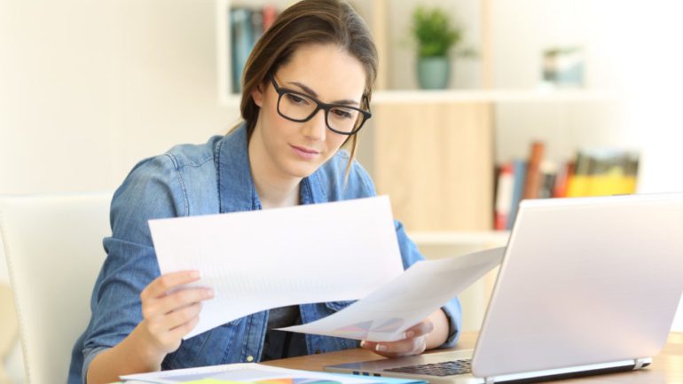 New homeowner comparing closing documents for storage on a table with her laptop open.