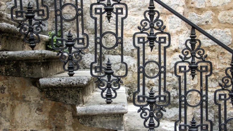 Elegant wrought iron bannister on outdoor steps of a stone front home.