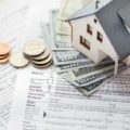 Photo of model home sitting on top of cash and tax documents show the tax benefit of selling a home.
