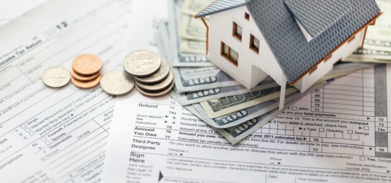 Photo of model home sitting on top of cash and tax documents show the tax benefit of selling a home.