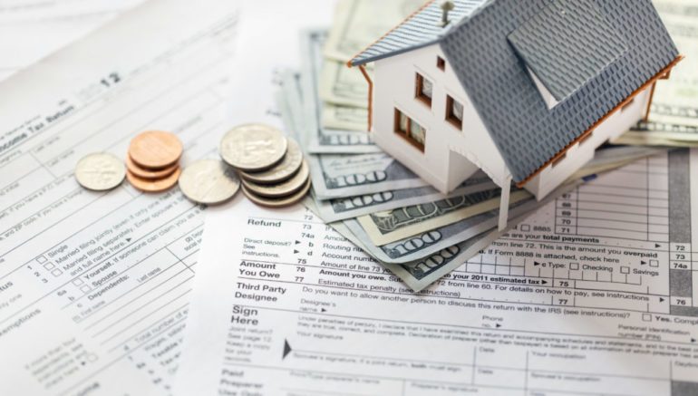 Photo of model home sitting on top of cash and tax documents show the tax benefit of selling a home.