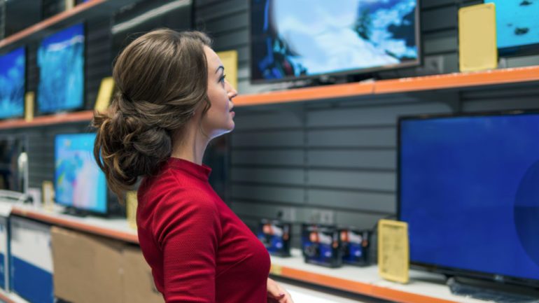 Smart modern female customer choosing large TV-sets at electronics store. She is looking for February's best buys for the home.