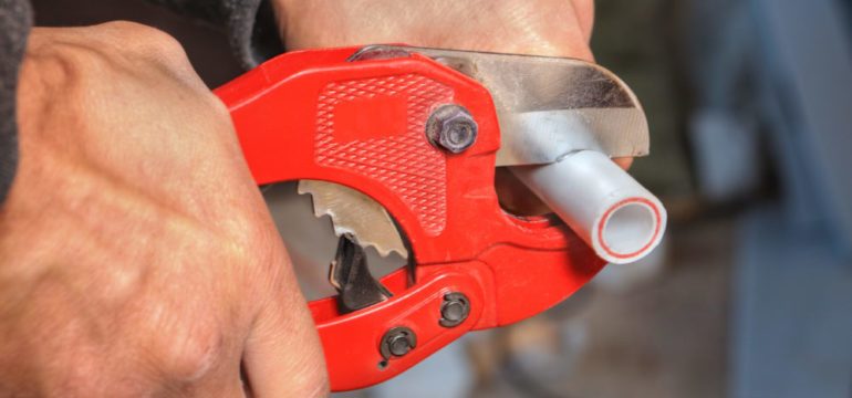 Polybutylene plumbing being cut by a plumber with a red pipe cutter.