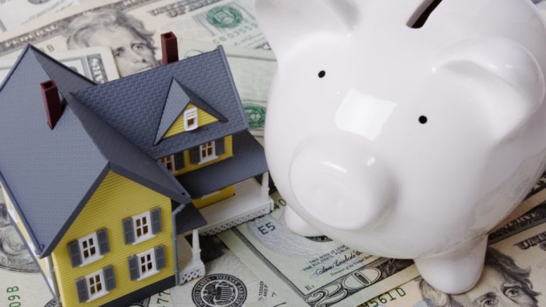 House with twenty dollar bills background and piggy bank for down payment assistance on a new home.