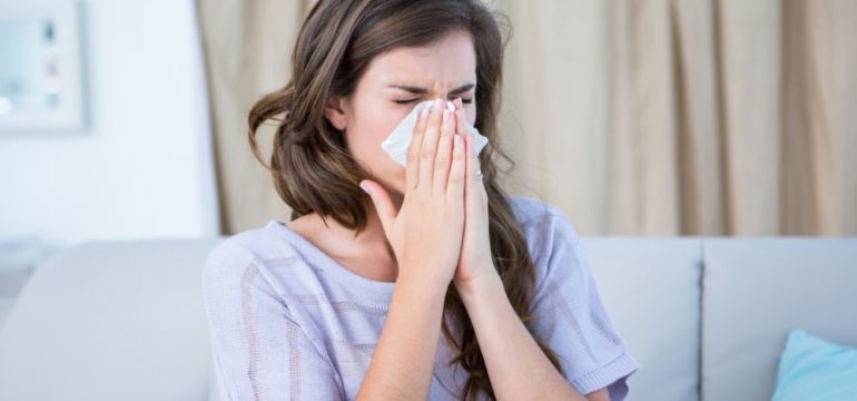 A woman blowing her nose due to an allergy in her home.
