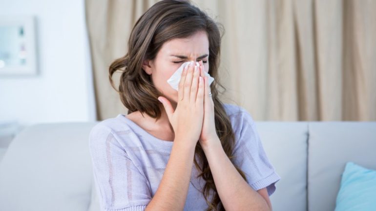 A woman blowing her nose due to an allergy in her home.