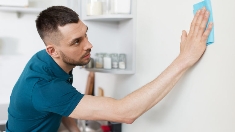 A man with cloth cleaning marks from walls in home kitchen.