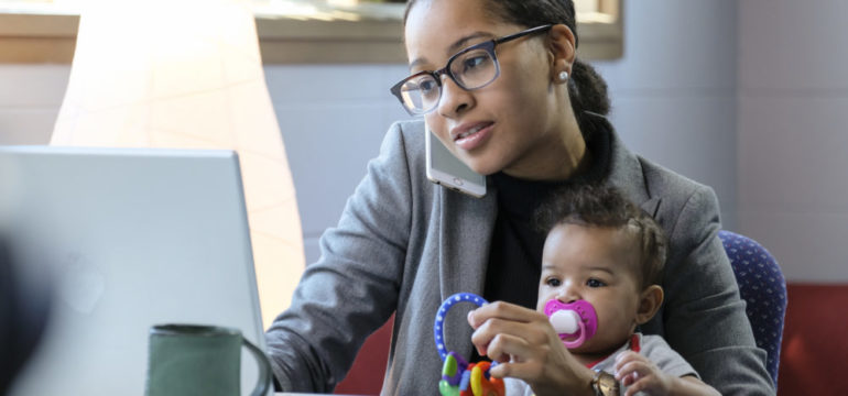 Mother holding baby and working at her computer in on her home business.