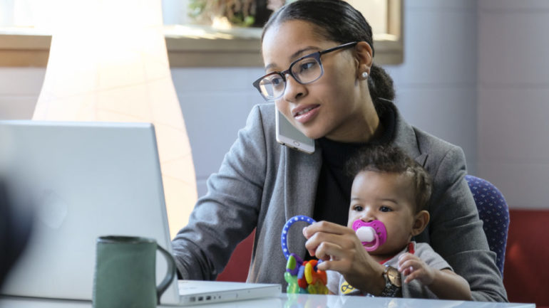 Mother holding baby and working at her computer in on her home business.