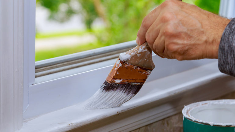 Painting wooden windows with paintbrush while windows may get stuck when the trim dries.