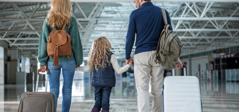 Glad parents and child passing terminal after plane landing. They are waiting for their shipped belongings for their new home.